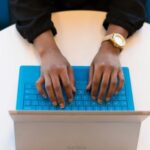 brown-skinned-hands-with-gold-wrist-watch-tying-on-a-blue-keyboard.jpg.optimal.jpg