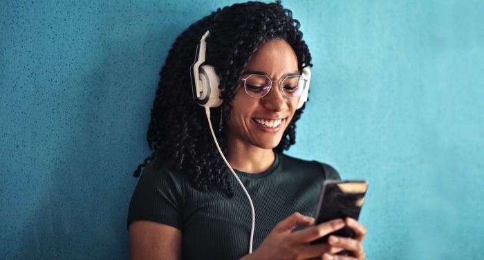 light-brown-skinned-Black-woman-with-thick-curly-hair-is-wearing-headphones-looking-at-her-phone-and-smiling.jpg.optimal.jpg